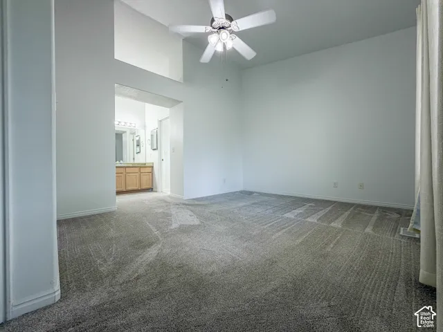 Expansive carpeted room with vaulted ceilings, a ceiling fan, and an arched entry leading to a bathroom with a wood-finish vanity