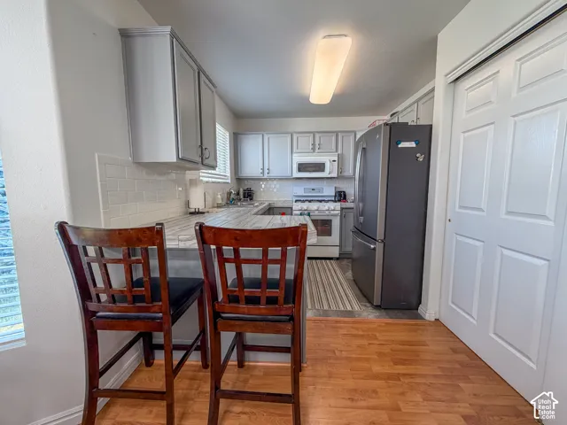 Kitchen featuring wood-finish flooring, white subway tile backsplash, white cabinetry, and stainless steel appliances