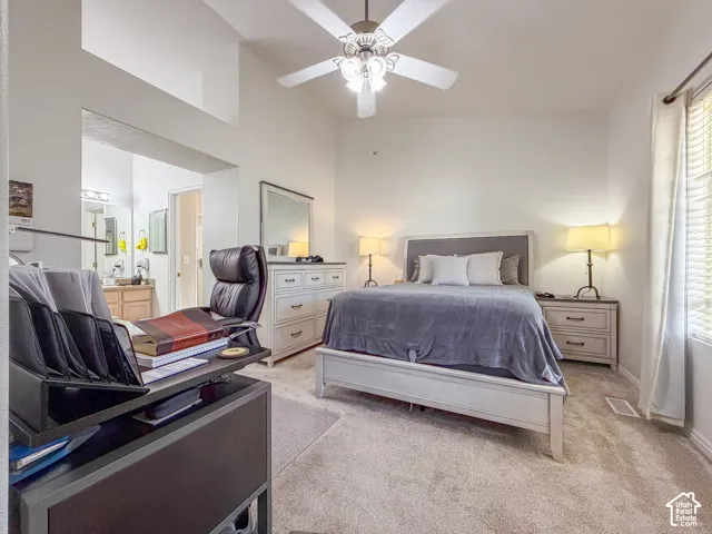 Vaulted ceiling with ceiling fan, plush carpet flooring, window with blinds, and built-in vanity with dual sinks visible in the background