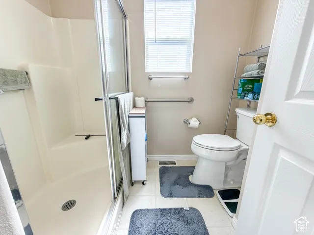 Walk-in shower with sliding glass door, white toilet, and window with blinds