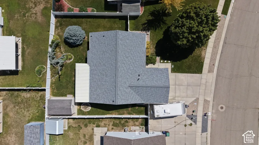 Asphalt shingle roof, paved driveway, concrete sidewalk, mature trees, and fenced backyard