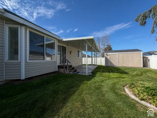 Expansive grassy yard with a covered patio, vinyl fencing, and a detached storage shed