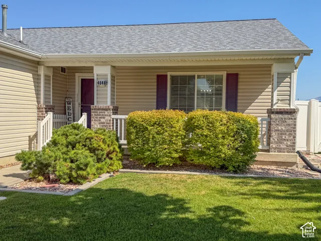 Inviting facade featuring horizontal siding, a covered porch with brick-clad columns, a dark-toned entry door, and a well-maintained lawn with established shrubbery