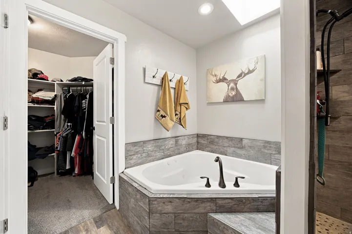 Corner soaking tub with dark bronze fixtures, skylight, and wood-look tile surround