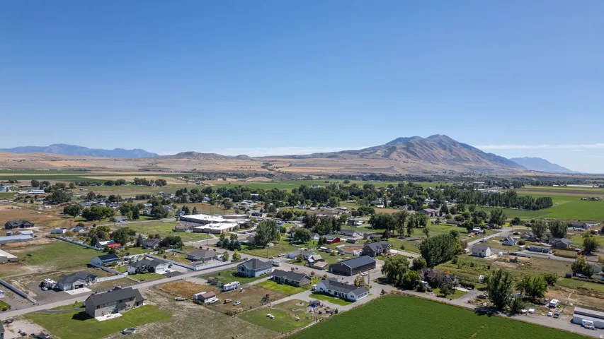 Expansive rural landscape featuring residential properties, agricultural fields, and distant mountains under a clear sky