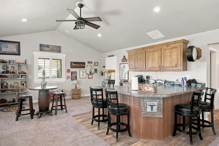 Vaulted ceiling with a ceiling fan, recessed lighting, wood-finish flooring, light-toned cabinetry, and a countertop with an integrated bar