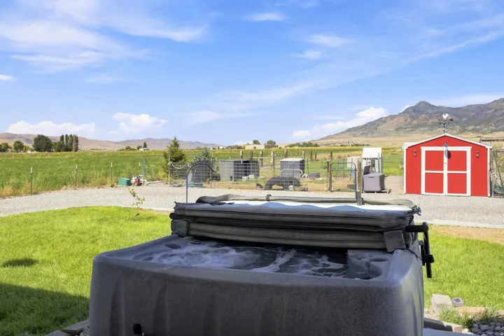 Outdoor spa with bubbling water, gravel hardscaping, expansive green lawn, and a red storage shed with a weather vane