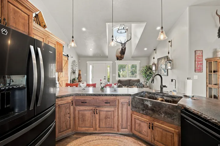 Kitchen featuring wood cabinetry, stone countertops, a large farmhouse-style sink, a black refrigerator, and pendant lighting