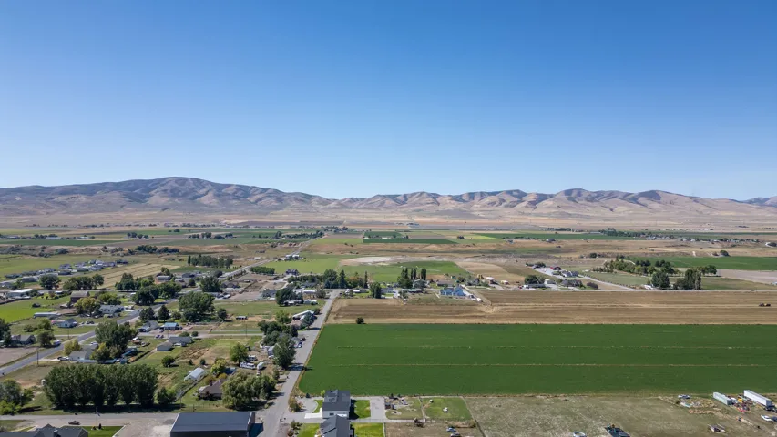 Expansive rural landscape with agricultural fields, scattered residential structures, mature trees, and distant mountain ranges