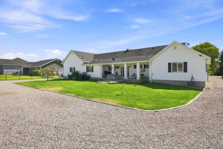 White siding exterior with black shutters, covered porch, dark shingle roof, and a gravel driveway