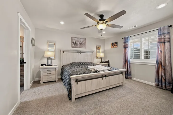 Spacious primary bedroom featuring a wood-finish bed frame with paneled headboard and footboard, coordinating wood nightstands, ceiling fan with integrated lighting, recessed ceiling lights, and carpet flooring