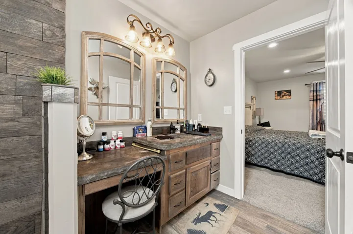 Wood-finish plank wall accent, dual framed mirrors with overhead vanity lighting, integrated vanity counter with basin, wood-finish cabinetry, and wood-finish flooring
