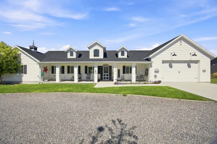 White siding exterior with a dark asphalt shingle roof, featuring multiple dormer windows, a covered front porch with white columns, and an attached two-car garage