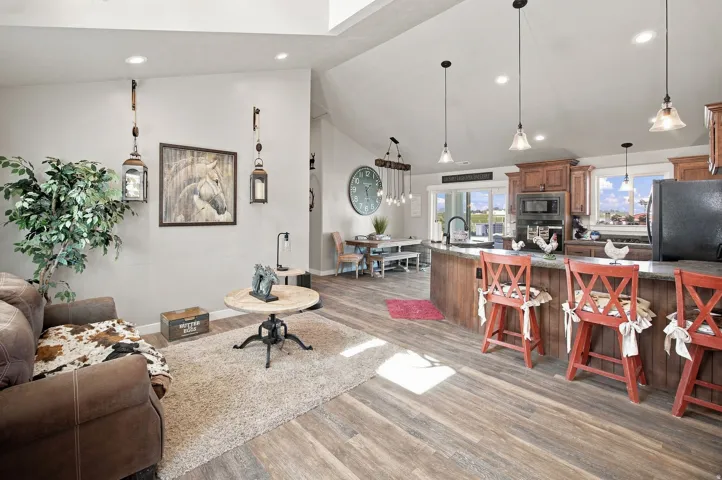 Open-concept living space featuring vaulted ceilings, wood-finish flooring, a kitchen island with built-in seating, and rich wood cabinetry