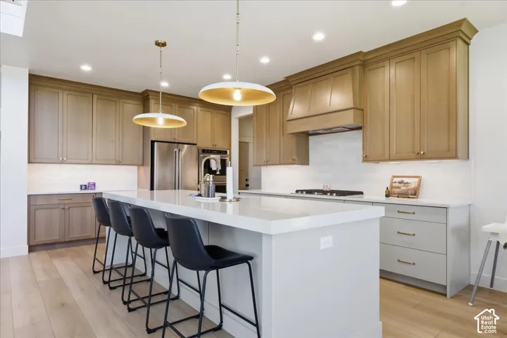 Kitchen featuring light wood-finish flooring, two-tone cabinetry, stainless steel appliances, a white tile backsplash, and a large center island with pendant lighting