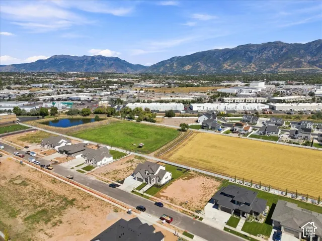 Mountain backdrop with prominent peaks, residential development with new construction, expansive green spaces, and a reflective water feature
