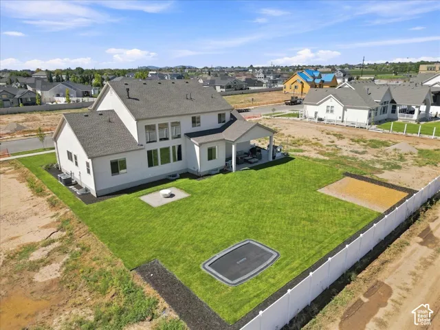 Expansive backyard featuring a manicured lawn, covered patio, and white privacy fencing