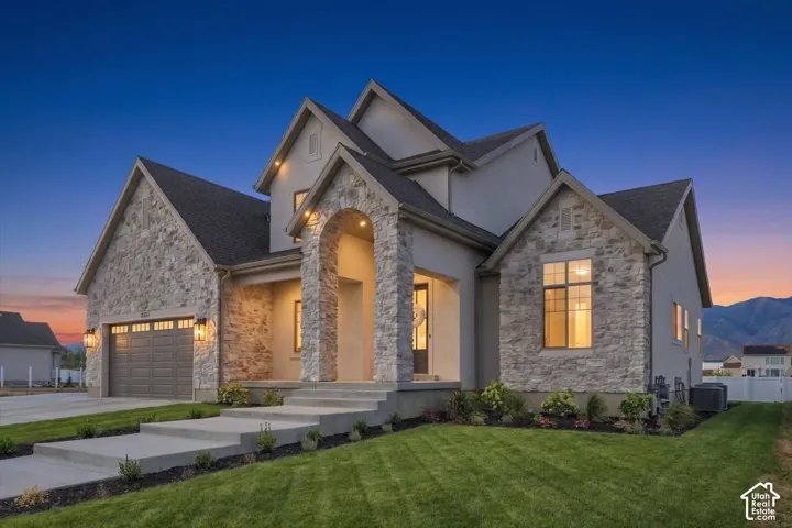 Stucco and stone facade with multiple gables, arched entry, concrete steps, and a two-car garage