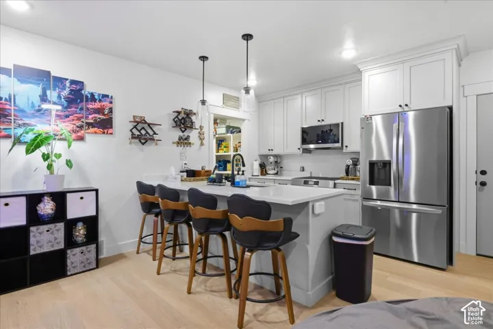 Kitchen featuring an island with seating, white cabinetry, stainless steel appliances, and wood-finish flooring