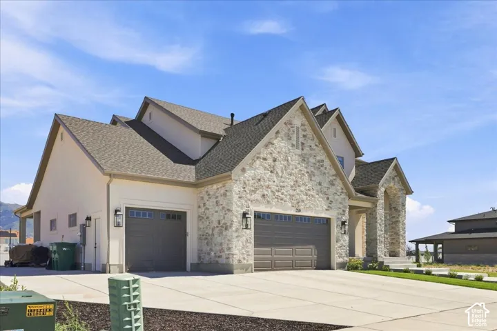 Contemporary exterior with a stone and stucco facade, a multi-car garage with panel doors, and a concrete driveway