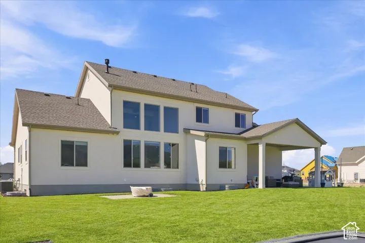 Expansive stucco exterior with a covered patio, multiple large windows, and a manicured lawn