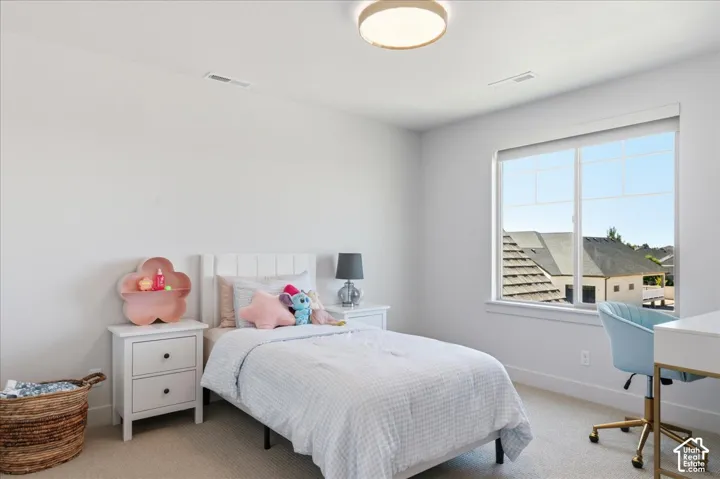 Recessed ceiling lighting, large window with roller shade, white headboard, matching nightstands with drawer storage, and light-toned carpeting