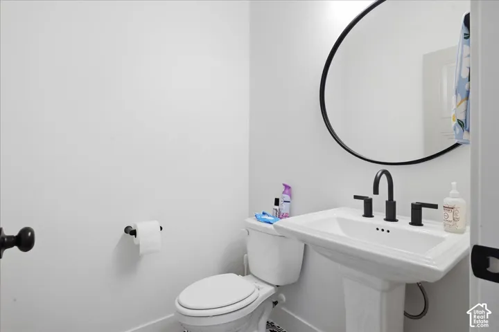 Pedestal sink with a matte black faucet, complete with a coordinated round mirror and toilet