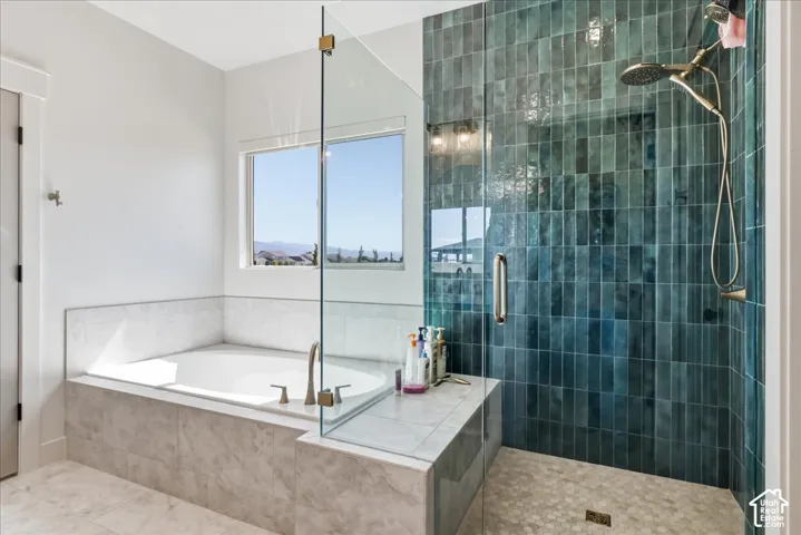 Built-in bathtub with a window, glass-enclosed shower with vertical teal tile, and a handheld showerhead