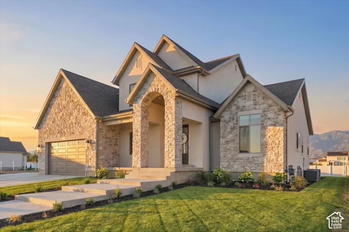 Stucco and stone exterior featuring a prominent arched entry, dark shingle roof, and an attached two-car garage