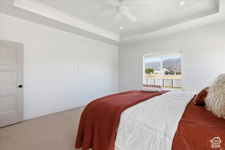 Recessed ceiling with an integrated fan, carpeted flooring, and a window framing a mountain backdrop