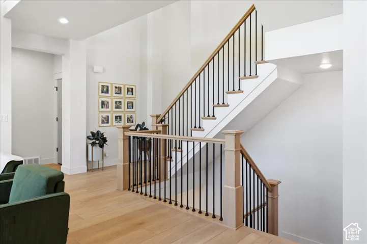 Hardwood flooring, open staircase with wood handrail, metal balusters, recessed lighting, and white walls