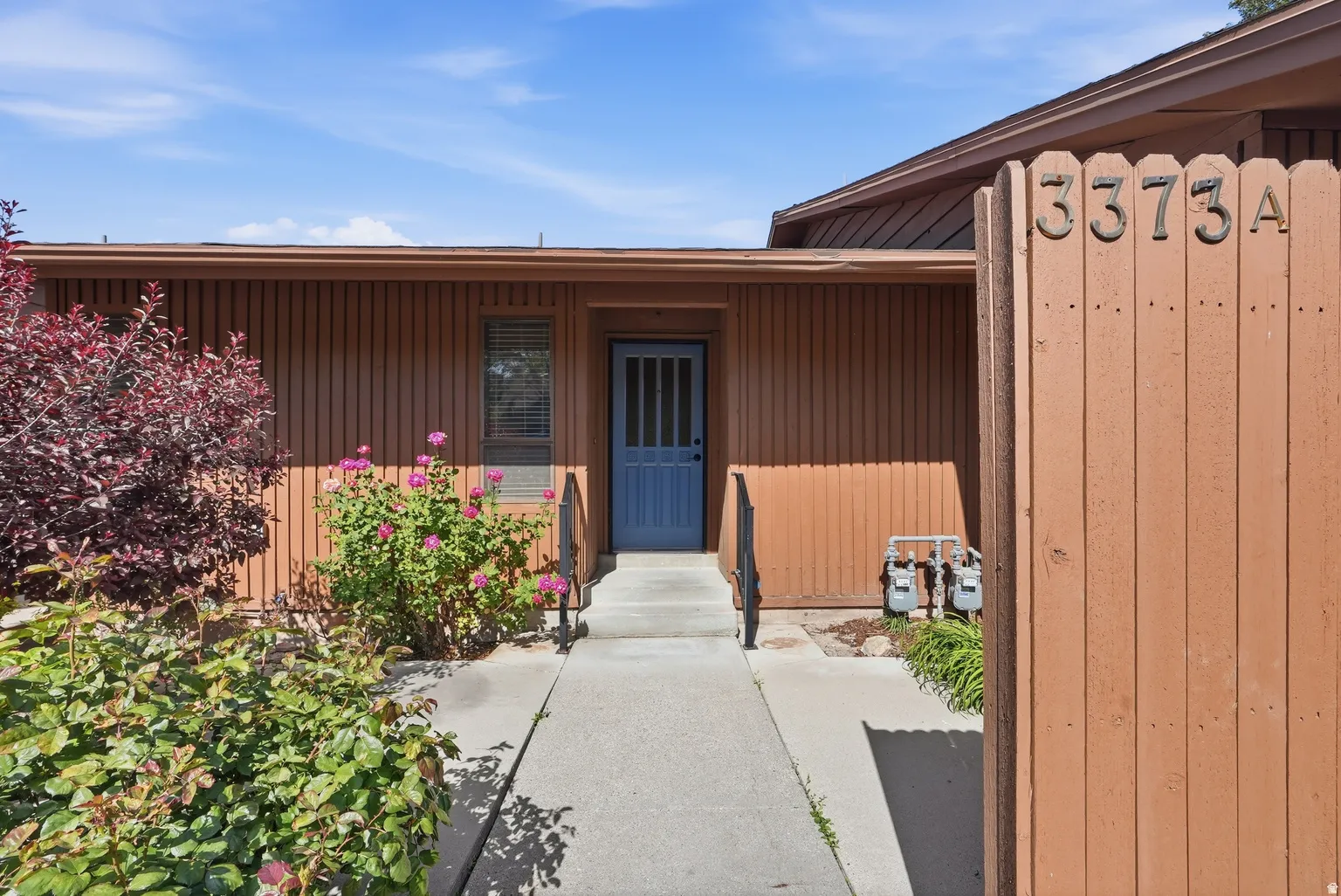 Wood-sided exterior with a blue paneled entry door, concrete walkway, and established landscaping