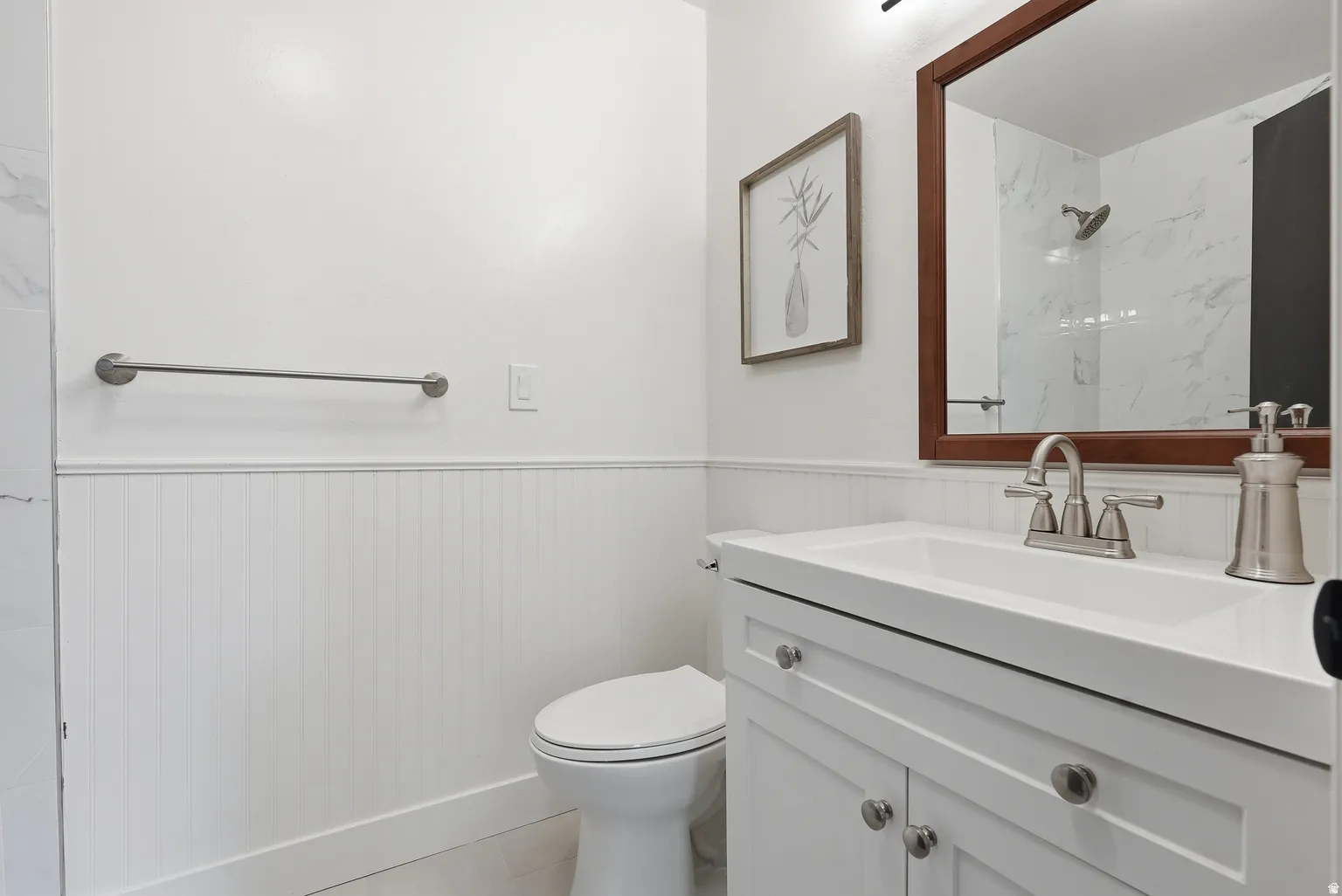 White vanity with a solid surface countertop, brushed nickel faucet, and beadboard wainscoting