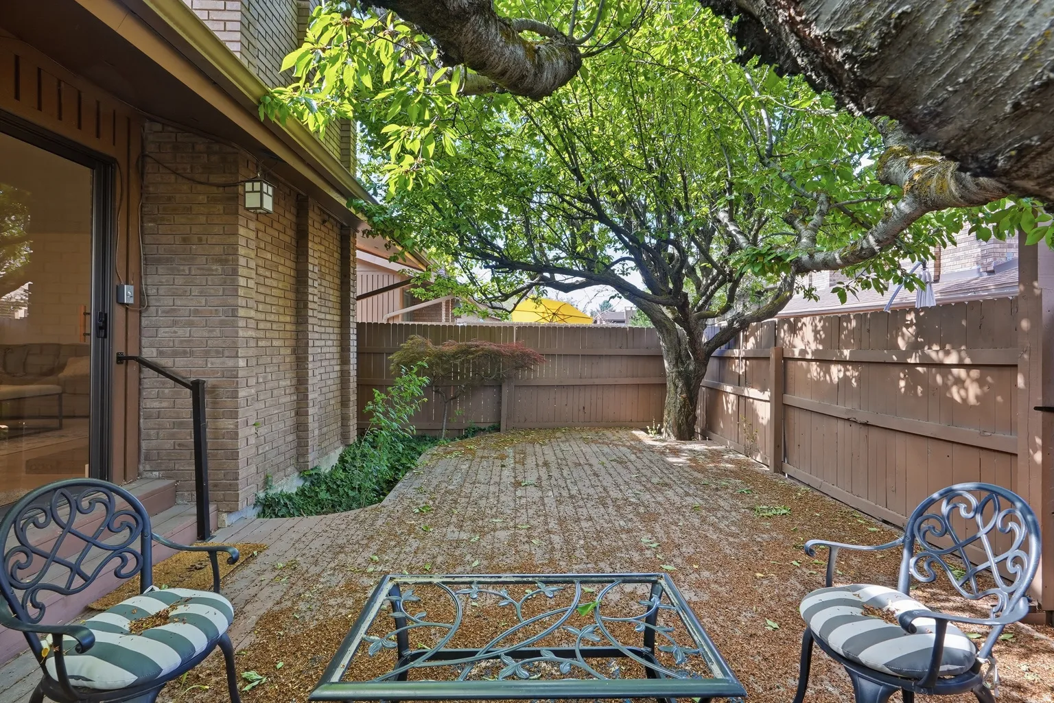 Private brick-paved patio with established perimeter fencing, mature tree, and brick exterior
