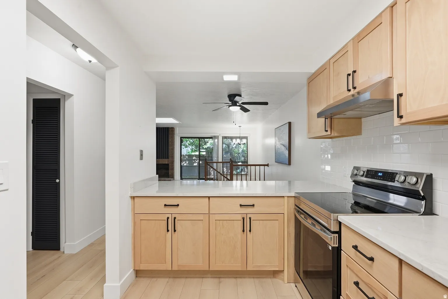 Light wood-finish cabinetry with matte black hardware, stainless steel electric range, white subway tile backsplash, and light-toned countertops