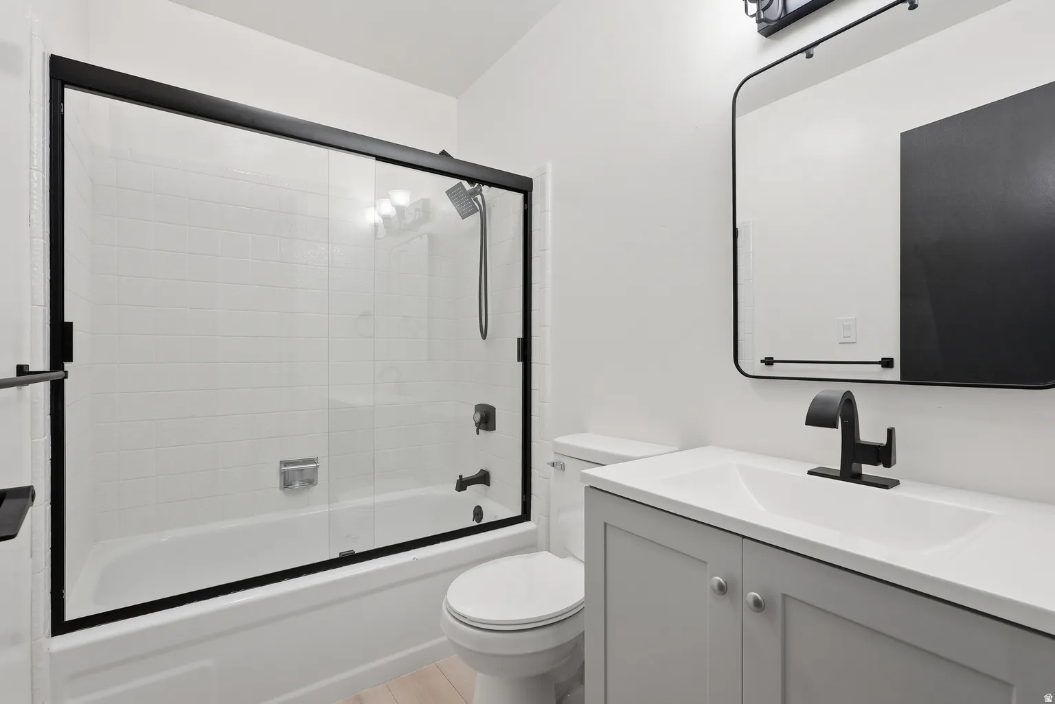 Glass-enclosed tub and shower combination with subway tile surround, gray vanity with integrated sink, matte black fixtures, and framed rectangular mirror