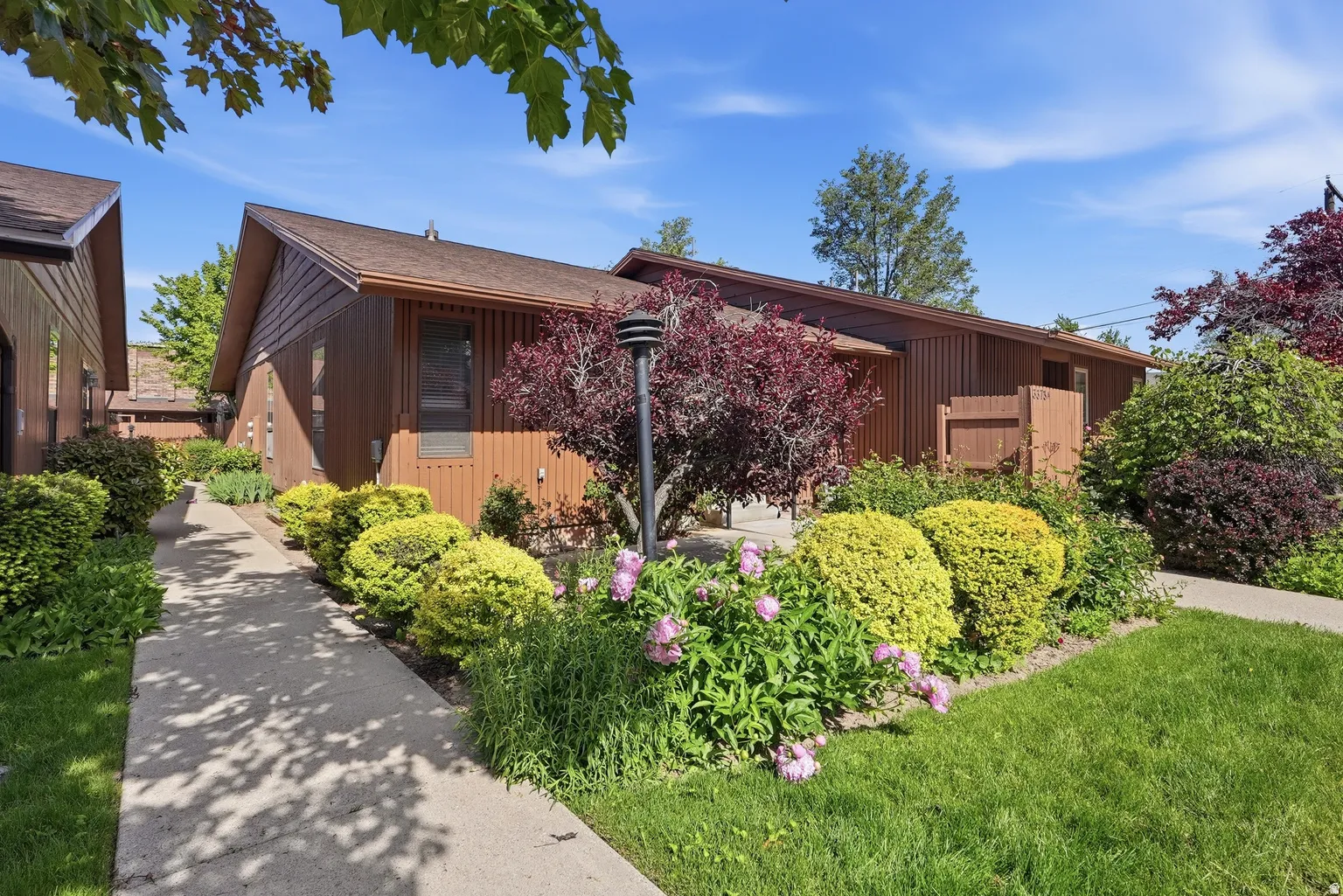 Wood-paneled exterior with an attached privacy fence, surrounded by mature landscaping, a paved walkway, and a manicured lawn