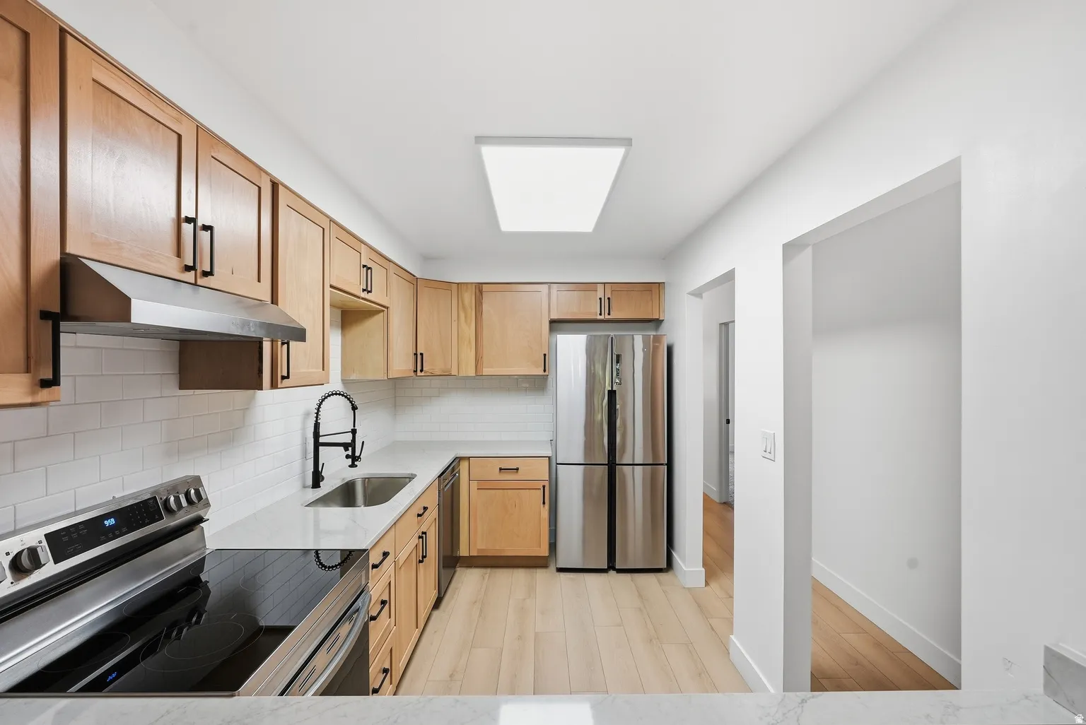 Kitchen featuring wood-finish cabinetry, stainless steel appliances, white subway tile backsplash, and light-toned wood-finish flooring