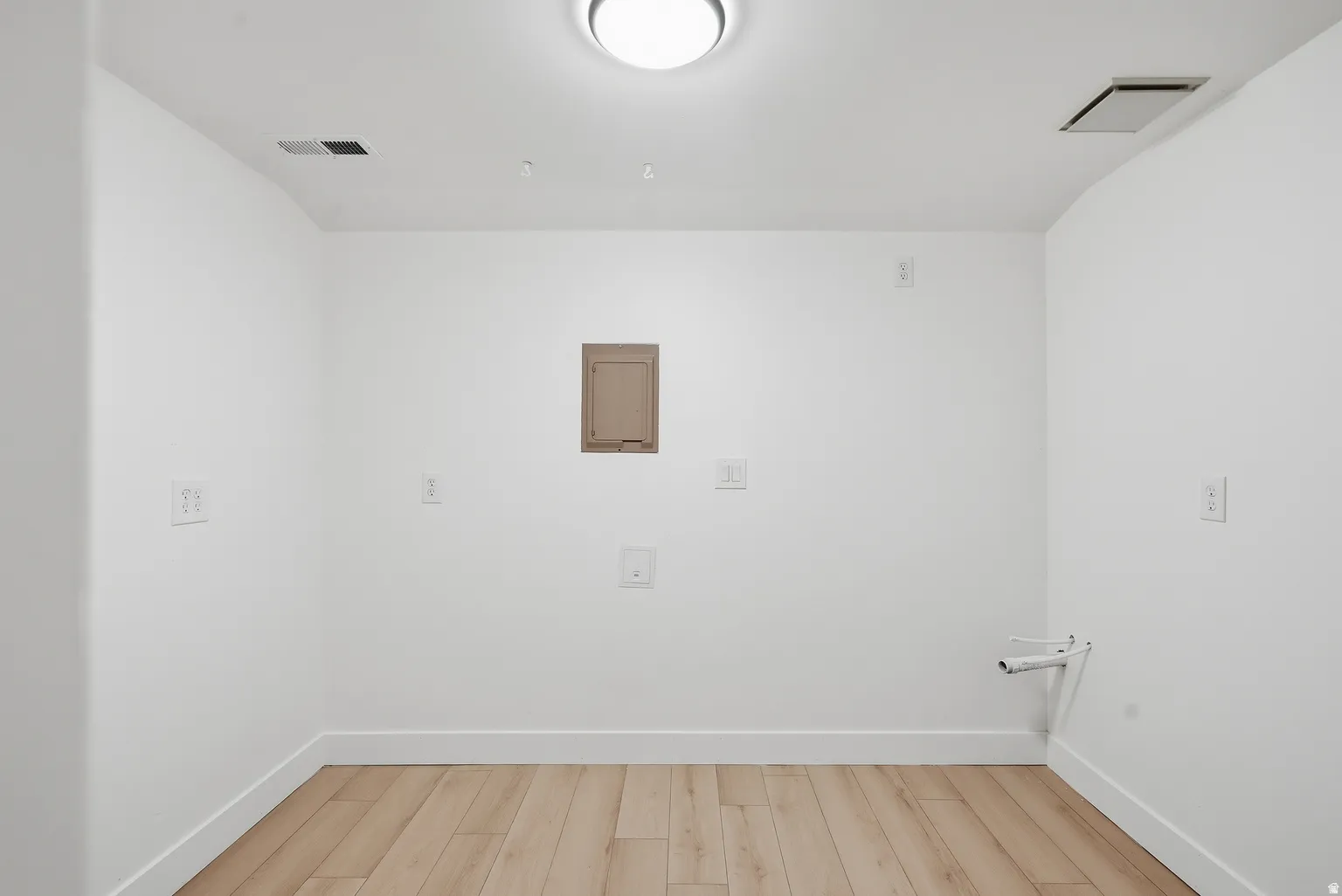 Wood-finish flooring with white baseboards, white walls, and a ceiling-mounted light fixture