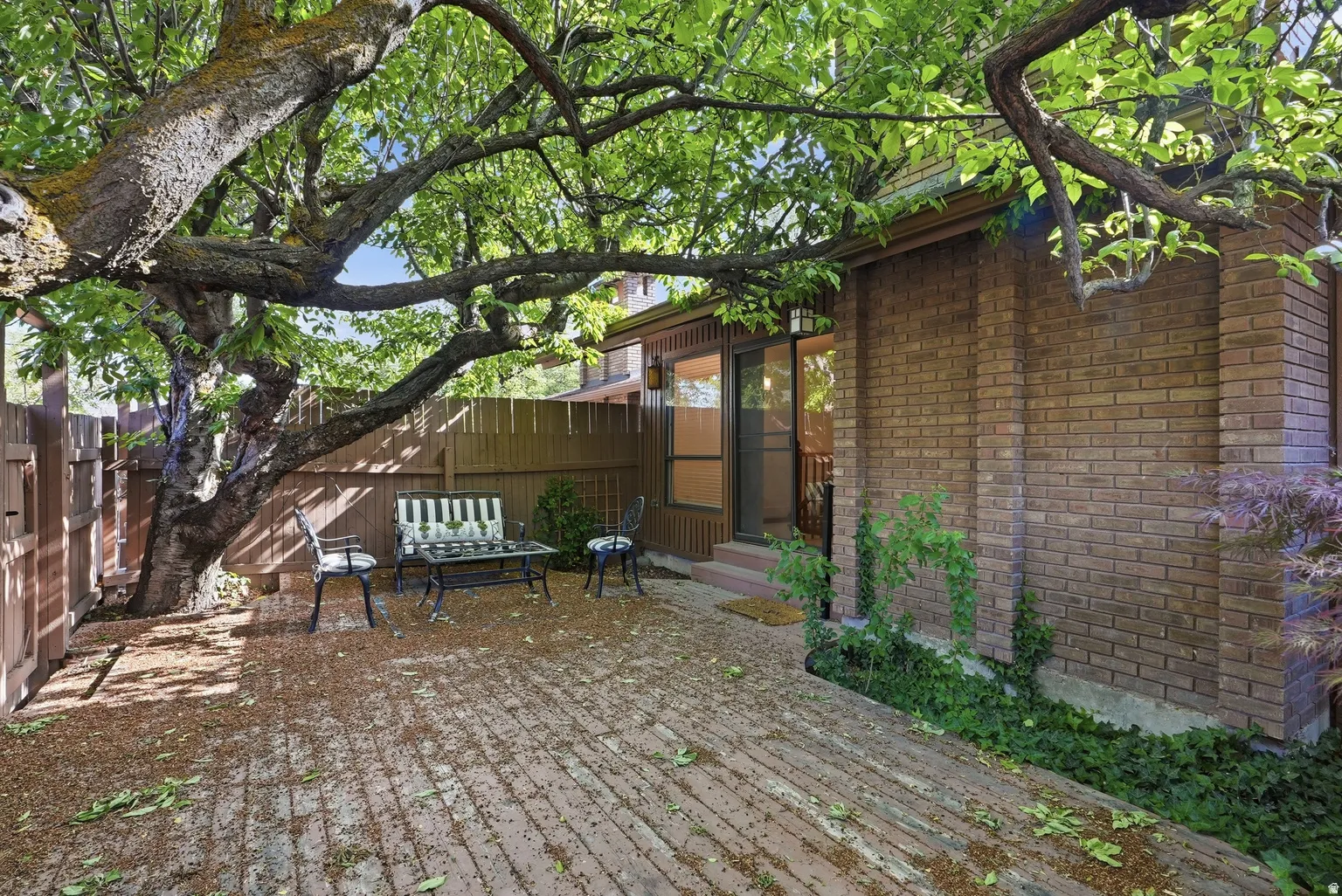 Brick exterior with sliding glass door access, surrounded by mature trees and a wood fence