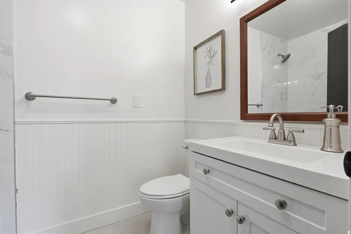 White vanity with a solid surface countertop, brushed nickel faucet, and beadboard wainscoting