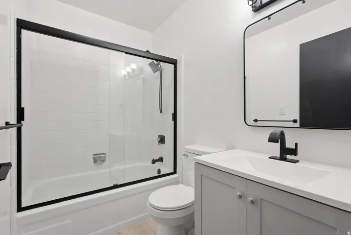 Glass-enclosed tub and shower combination with subway tile surround, gray vanity with integrated sink, matte black fixtures, and framed rectangular mirror