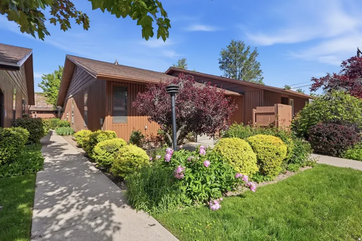 Wood-paneled exterior with an attached privacy fence, surrounded by mature landscaping, a paved walkway, and a manicured lawn