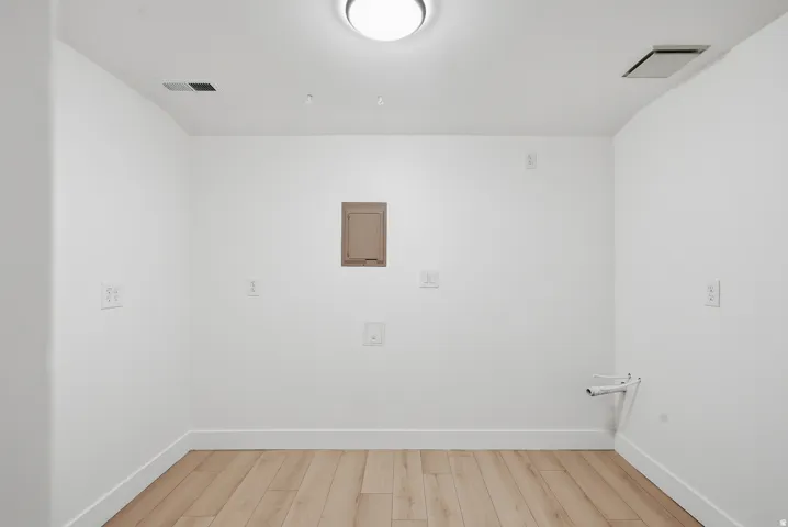 Wood-finish flooring with white baseboards, white walls, and a ceiling-mounted light fixture