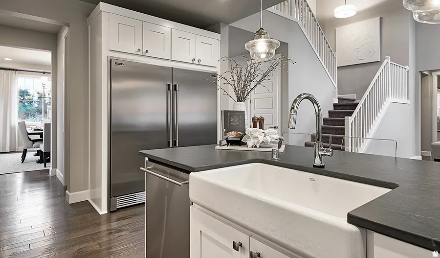 Kitchen featuring a farmhouse sink, stainless steel appliances, dark countertops, and white cabinetry