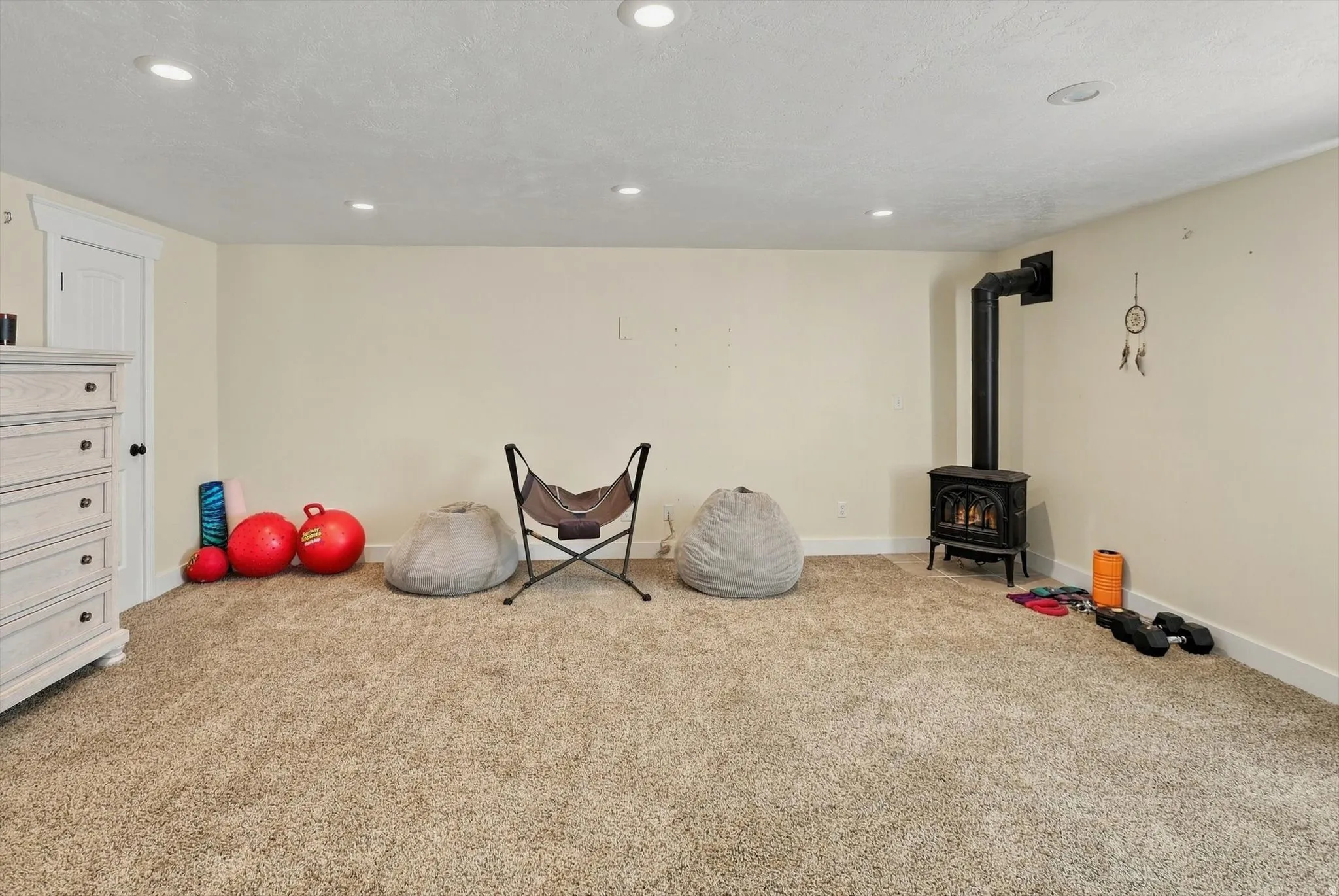 Carpeted flooring, recessed lighting, and a wood-burning stove with a black stovepipe