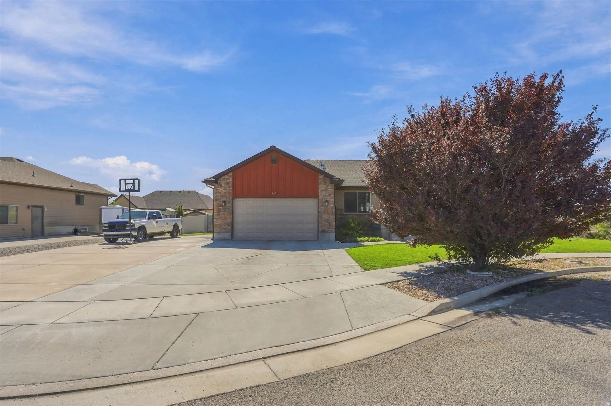 Stone and siding exterior with an attached garage, concrete driveway, and mature landscaping
