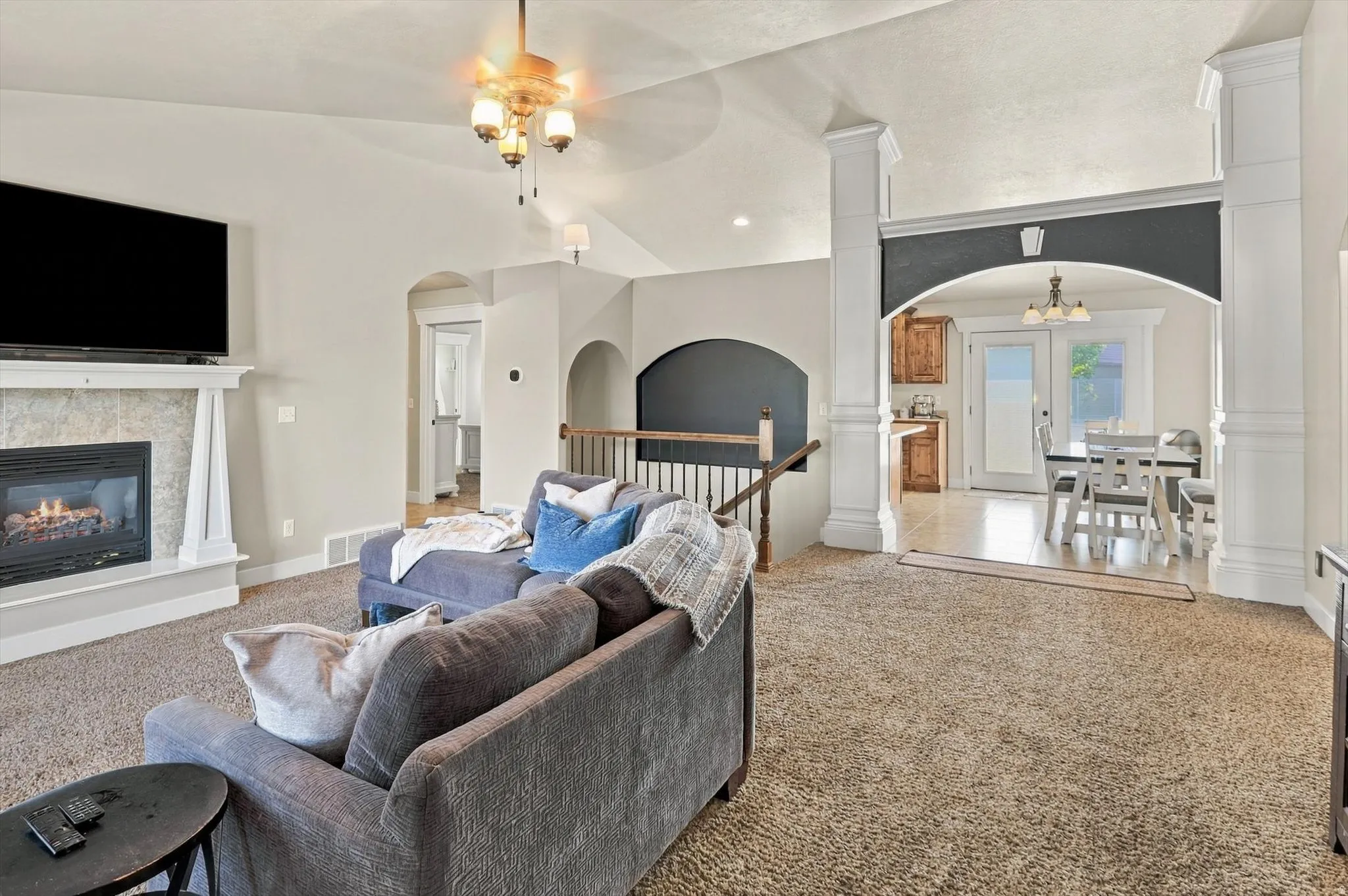Living area featuring a textured fireplace surround, white mantel, vaulted ceiling, and ceiling fan