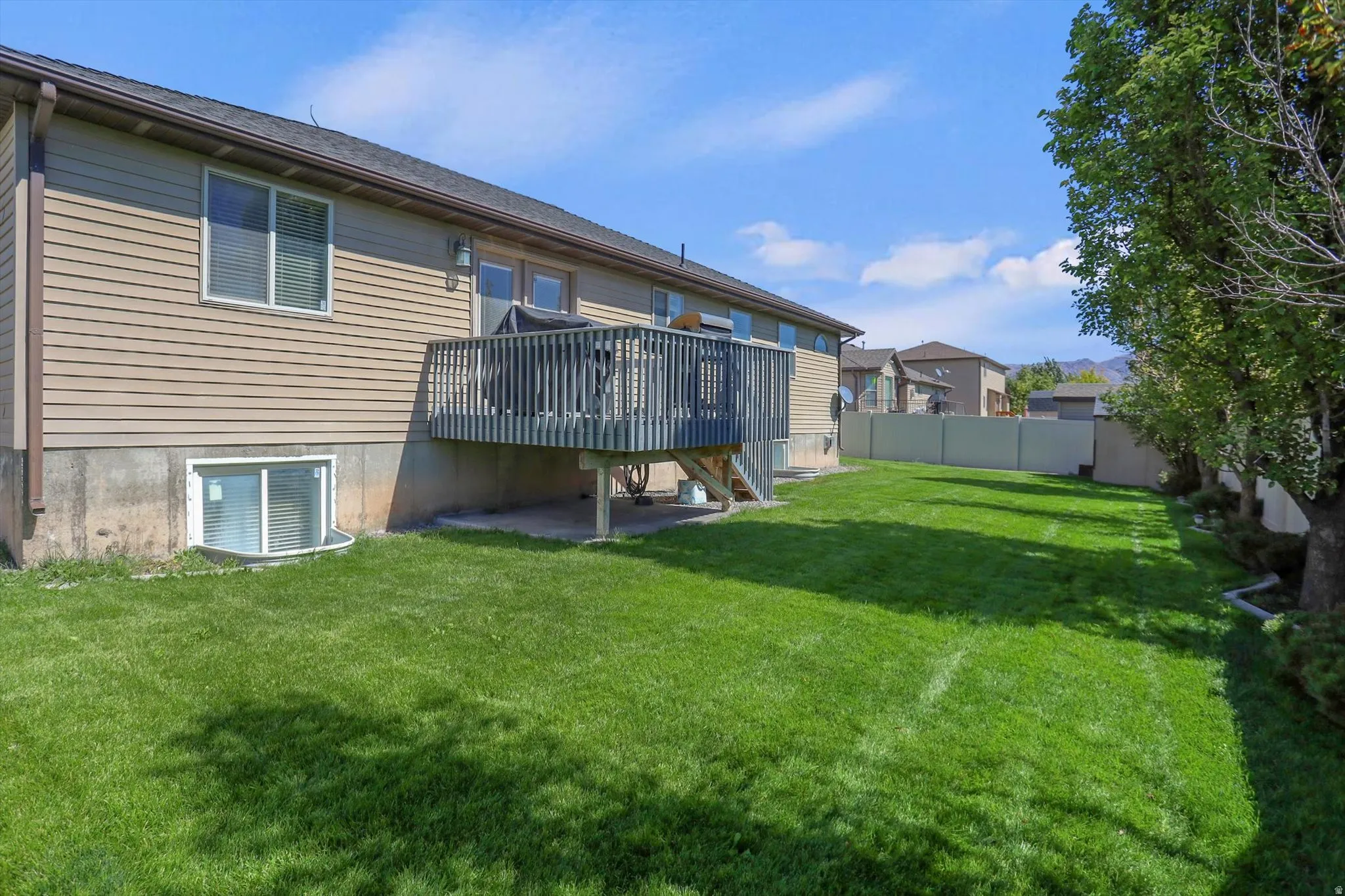 Expansive backyard featuring a manicured lawn, a two-story residence with tan siding, and a wood deck with railings