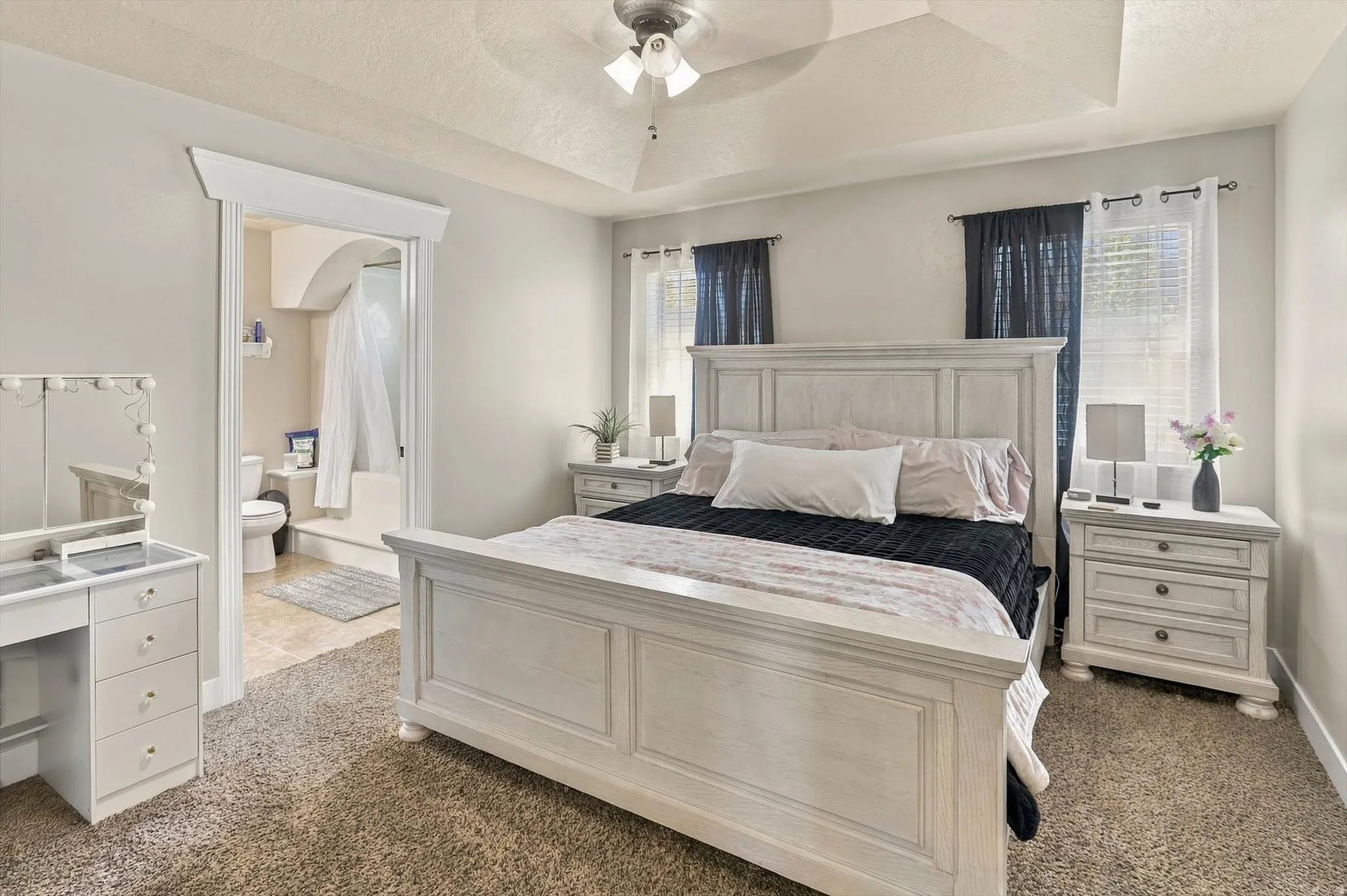Tray ceiling with a ceiling fan, carpeted flooring, and a doorway leading to a bathroom with a shower-tub combination